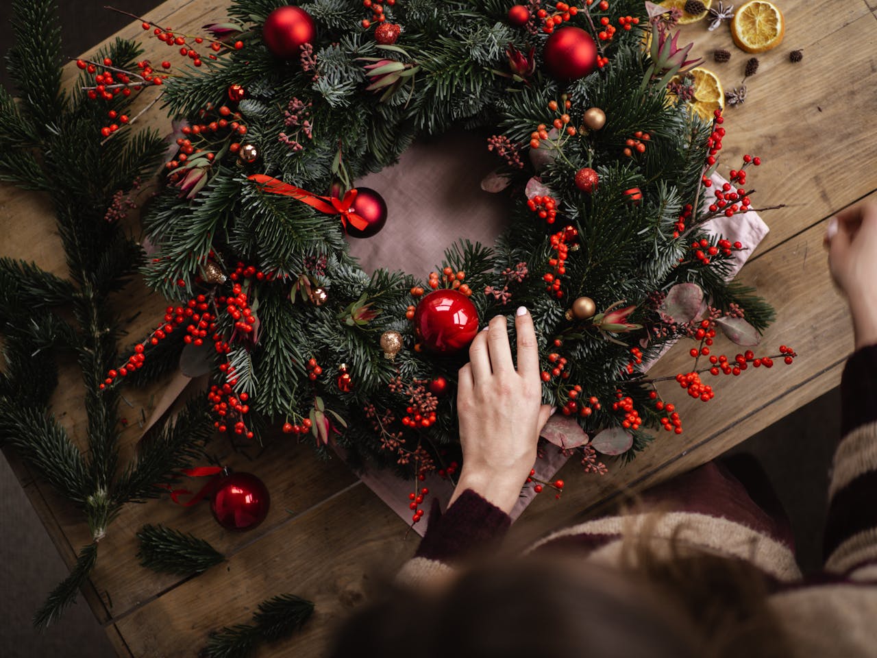 who-we-are Person adds decorations to festive Christmas wreath on wooden table.