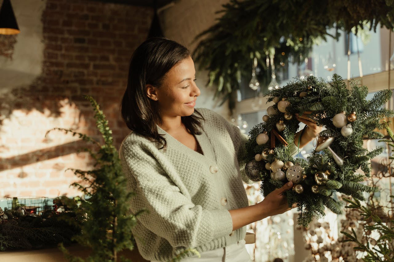 services-02 A woman admires a decorative Christmas wreath in a brightly lit room with festive holiday decor.