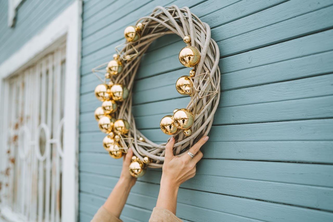 why-choose-us A person hangs a decorative gold ornament wreath on a vintage blue wooden wall.